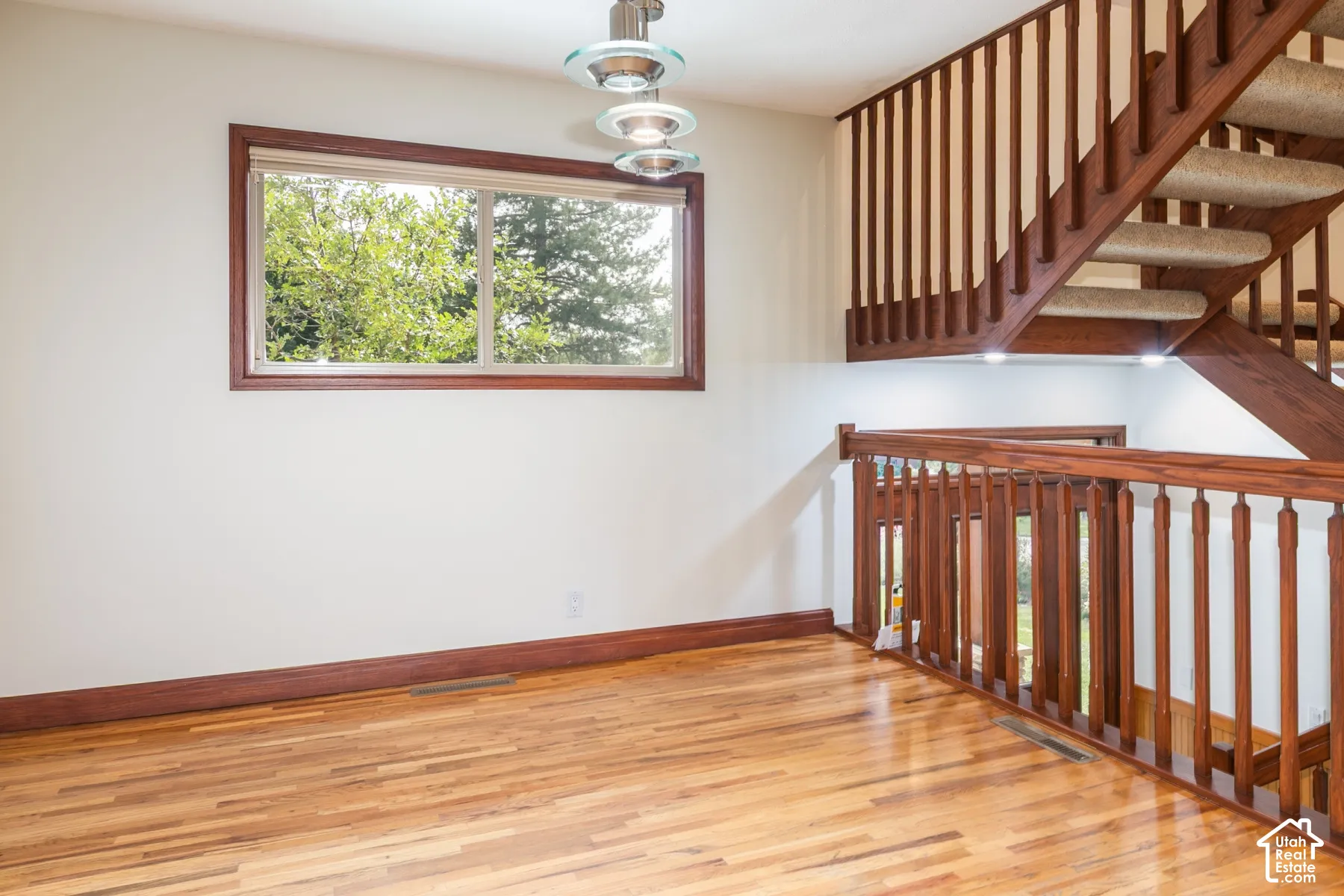 Hardwood flooring throughout, a large window with wood trim, and a contemporary pendant light fixture