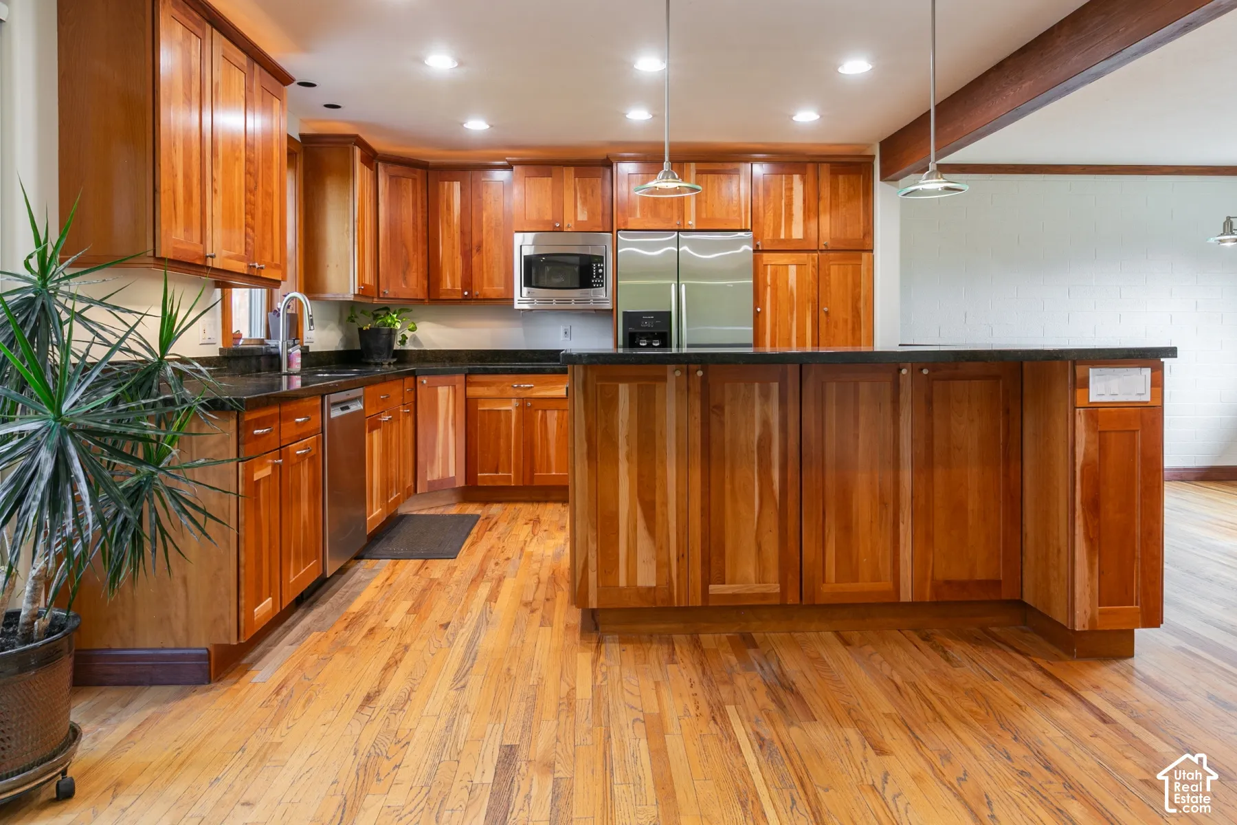 Kitchen featuring wood-finish cabinetry, stainless steel appliances, dark countertops, hardwood flooring, and recessed lighting