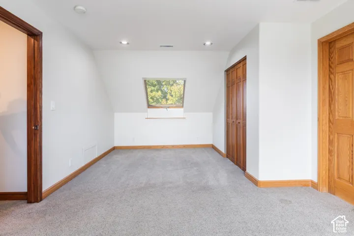 Room featuring light gray carpeting, white walls, natural wood-finish trim, and a window dormer