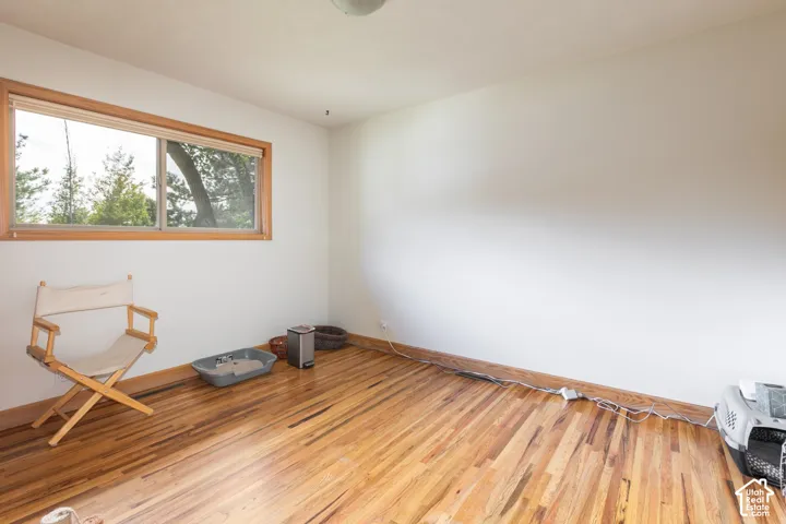 Wood-finish flooring with perimeter baseboards, a window with wood trim, and painted white walls