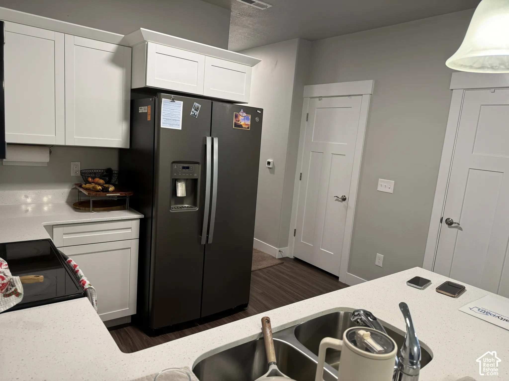 White shaker-style cabinetry with crown molding, light-toned countertops, a built-in stainless steel double sink, and wood-finish flooring