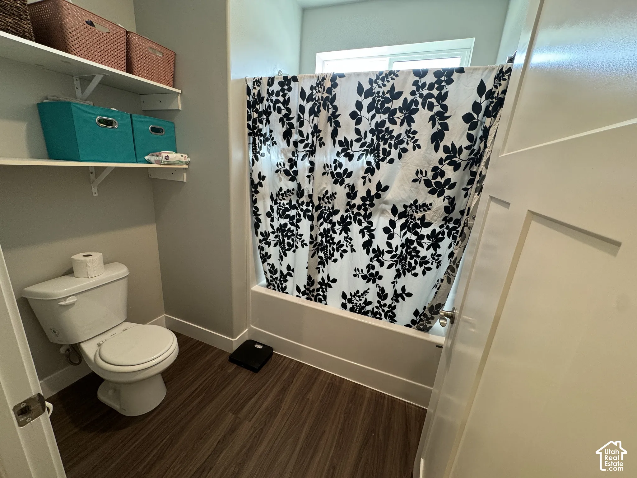 White bathtub with shower, wood-finish flooring, white toilet, and built-in shelving