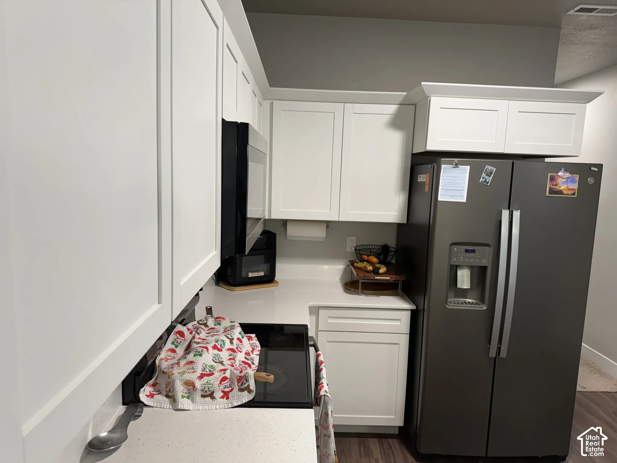 White shaker cabinetry, light-toned countertops, dark-finish refrigerator with ice and water dispenser, built-in microwave, wood-finish flooring
