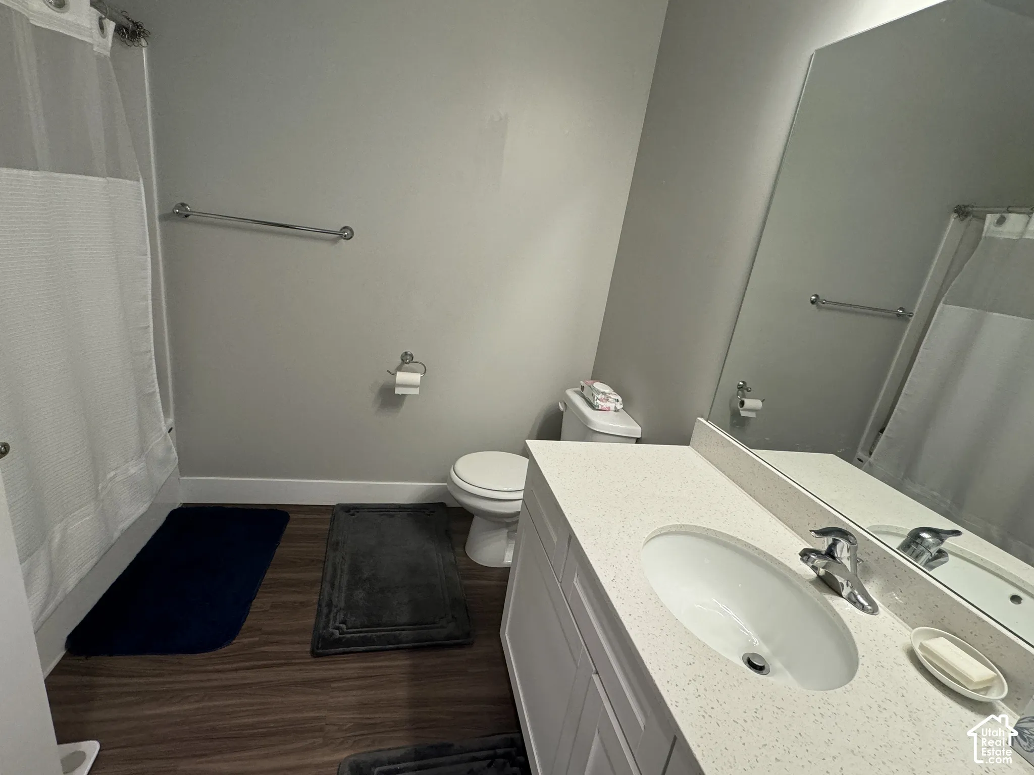 Vanity with integrated sink and chrome faucet, large frameless wall mirror, white toilet, and wood-finish flooring