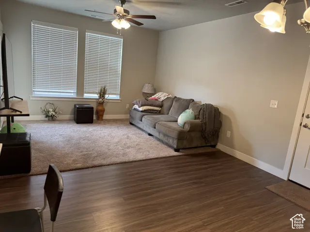 Spacious living area featuring wood-finish flooring, two large windows, a ceiling fan with integrated lighting, and neutral wall tones