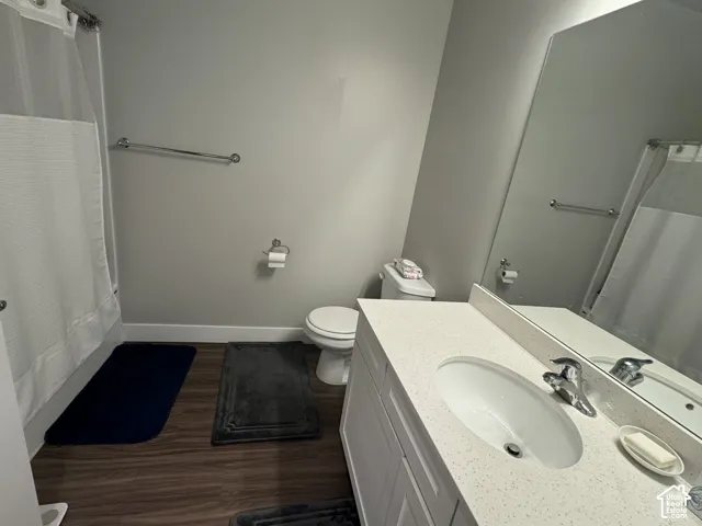 Vanity with integrated sink and chrome faucet, large frameless wall mirror, white toilet, and wood-finish flooring