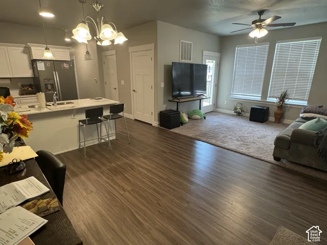 Open-concept living area featuring wood-finish flooring, a kitchen island with seating, white cabinetry, a ceiling fan, and large windows
