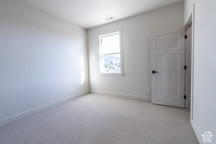 Spacious room featuring light carpeting, neutral wall color, white trim, a single window, and a three-panel interior door with matte black hardware