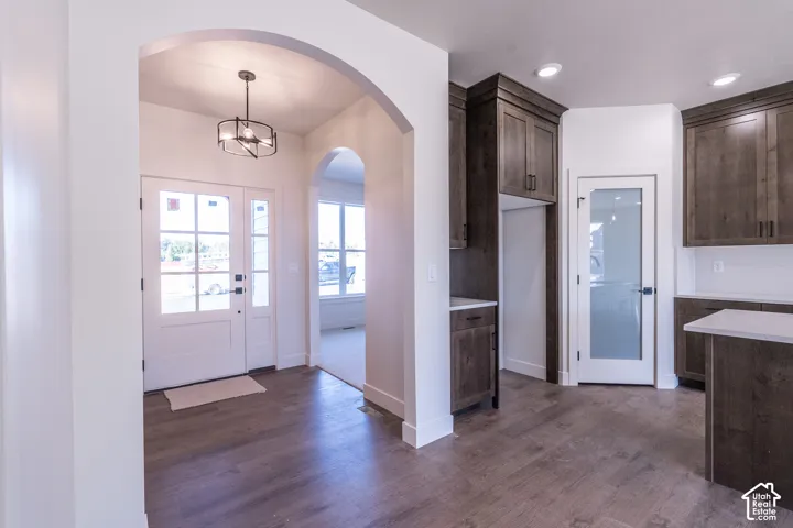Arched entryway with a decorative chandelier, dual paneled entry doors, wood-finish flooring, dark wood cabinetry, and solid surface countertops