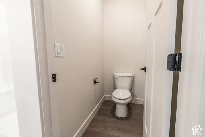 White toilet with a round bowl, wood-finish flooring, and white walls