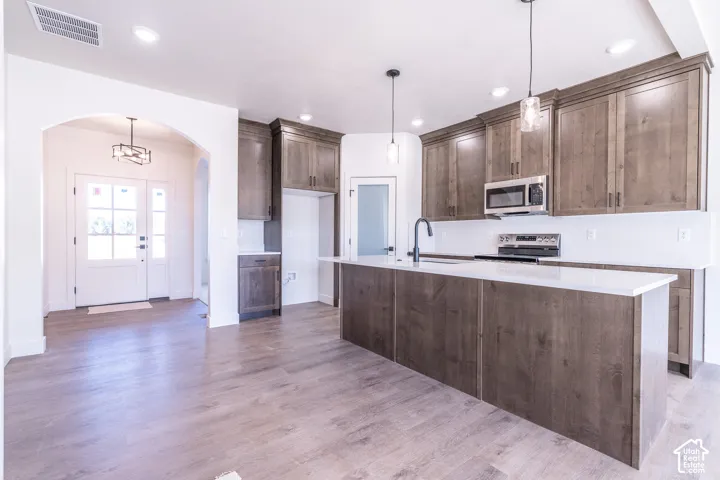 Open-concept kitchen featuring wood-finish flooring, recessed lighting, a large island with a light-toned countertop, and dark wood-finish cabinetry