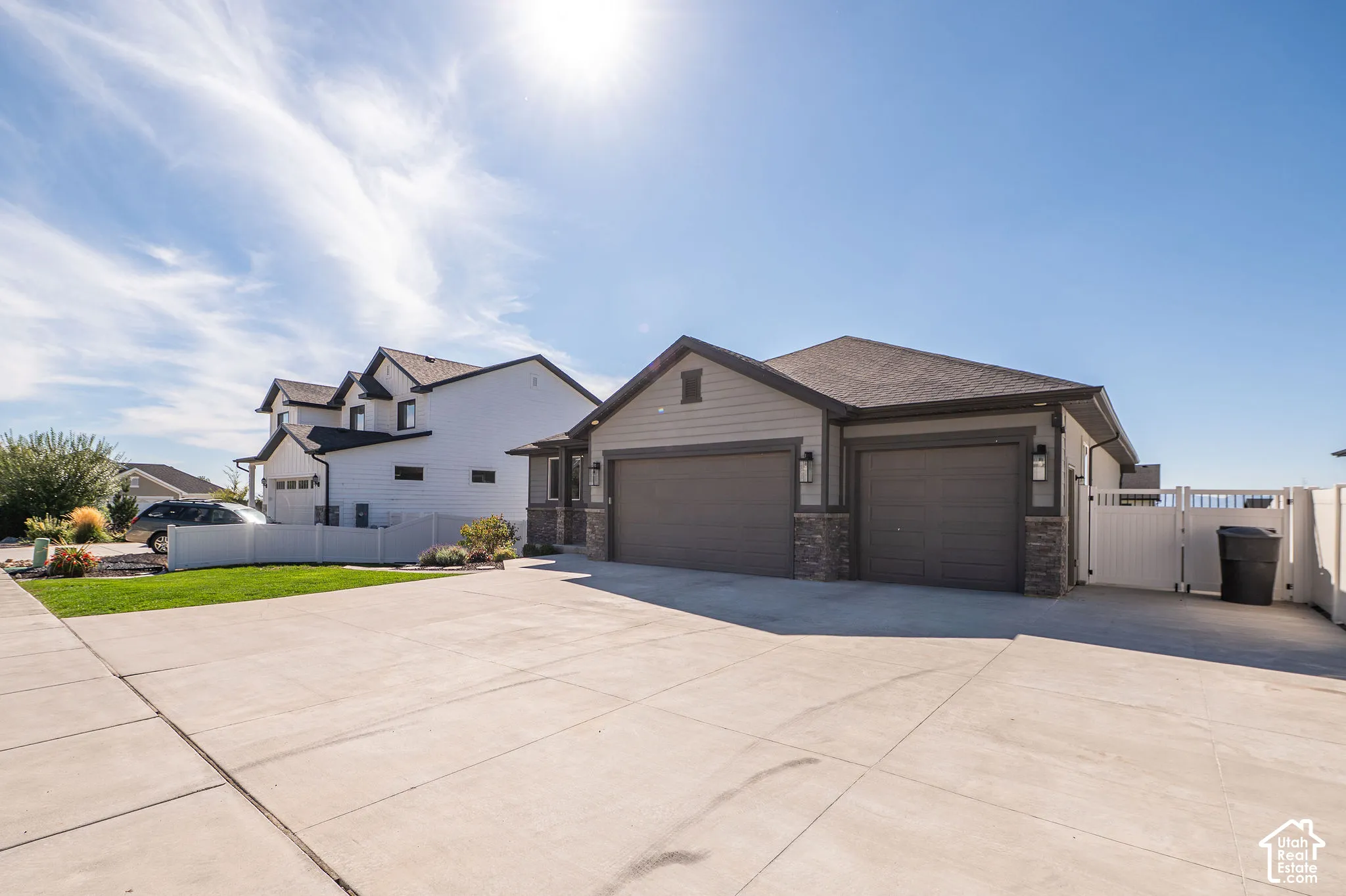 Expansive concrete driveway, two-car garage with overhead doors, stone accent columns, and a white privacy fence