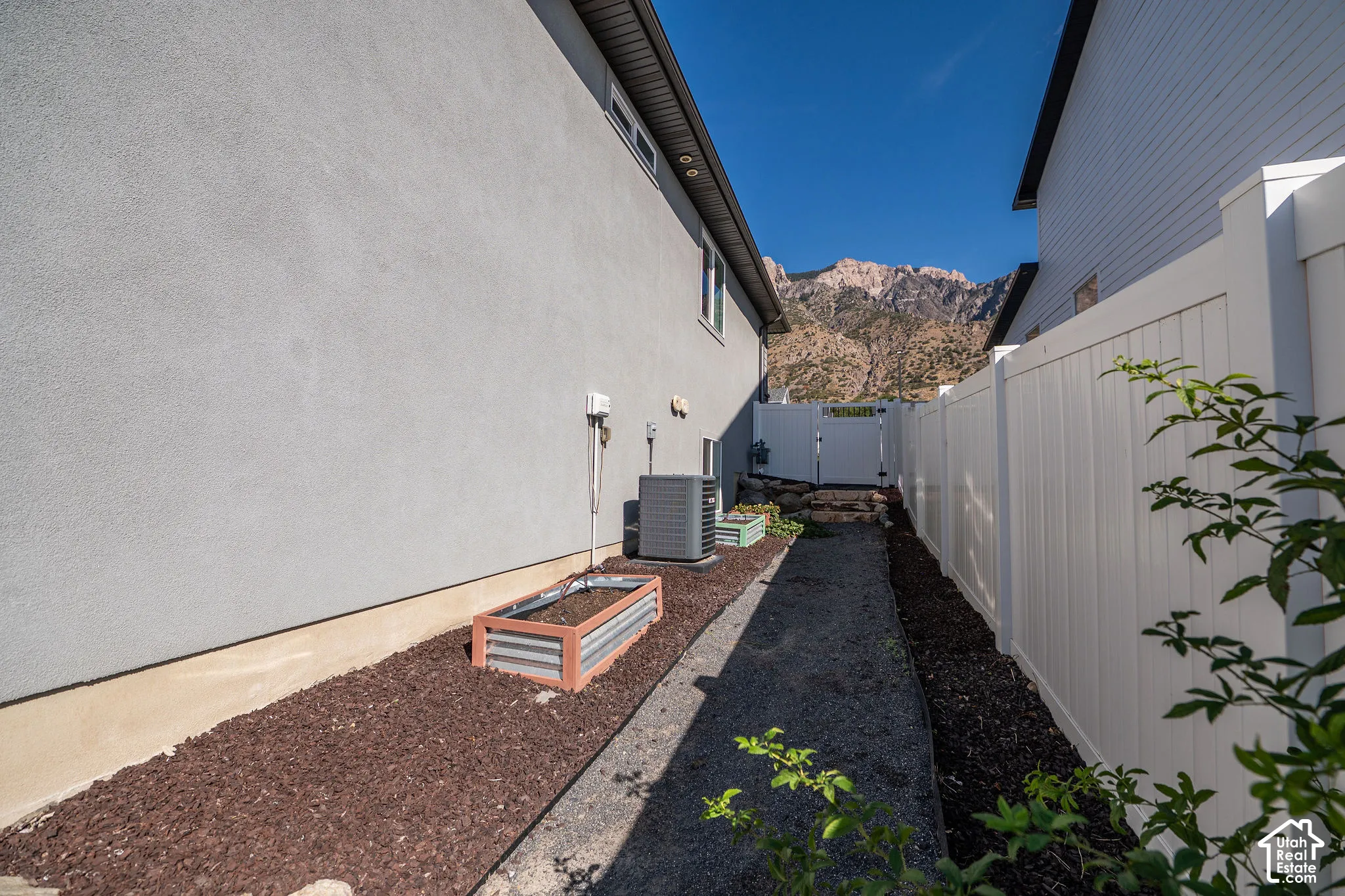 Stucco exterior with a modern raised garden bed, gravel pathway, and white privacy fencing