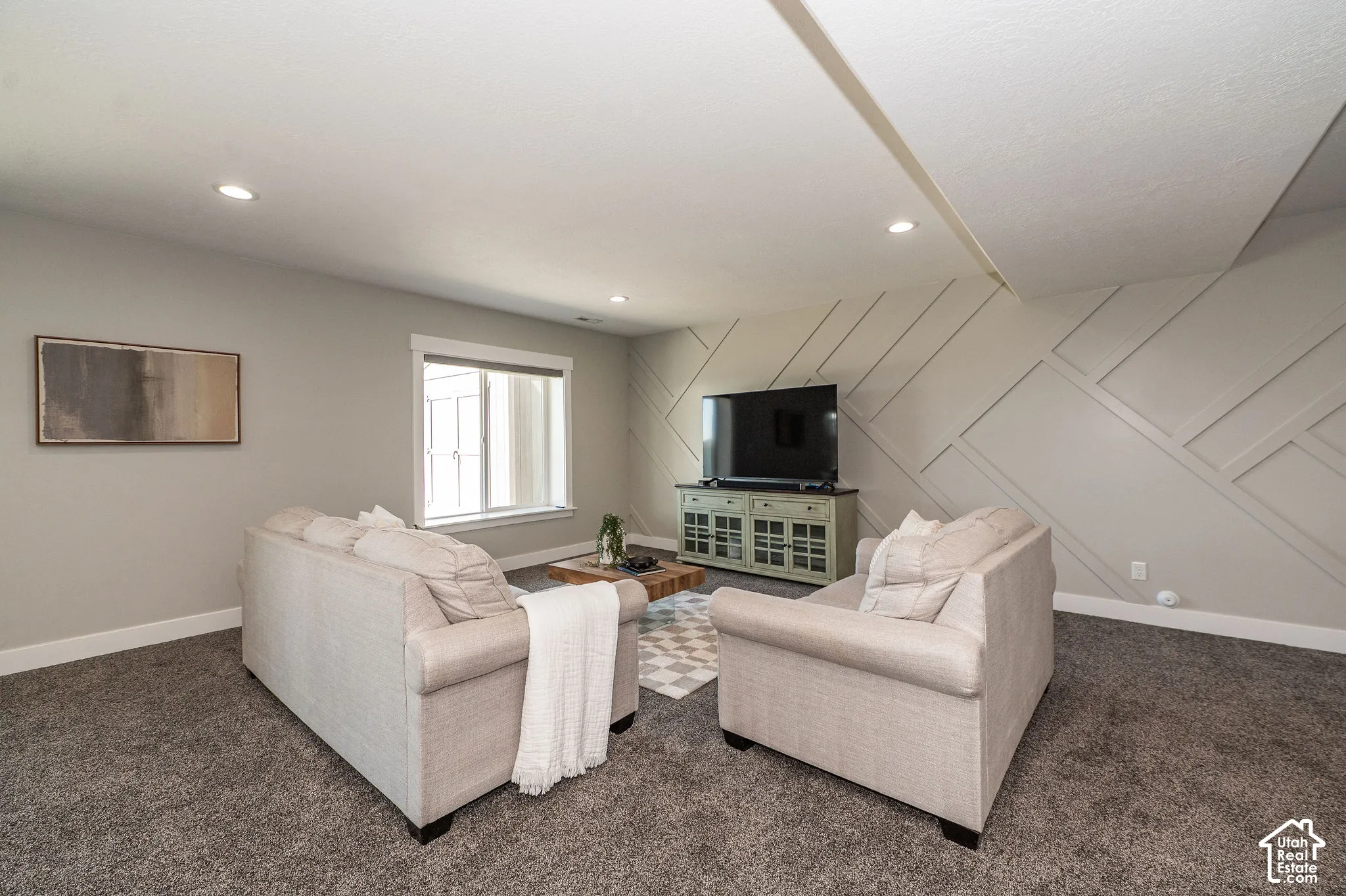 Recessed lighting, wall-mounted television, built-in media console, accent wall with geometric paneling, and a large window
