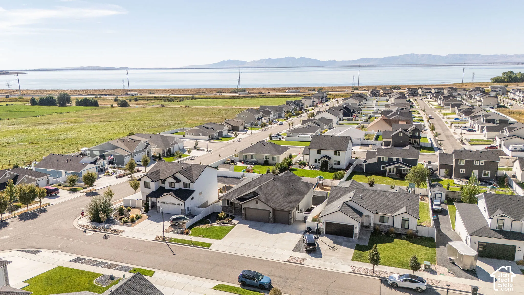 Expansive suburban development with manicured lawns and paved streets, featuring a prominent body of water and distant mountains