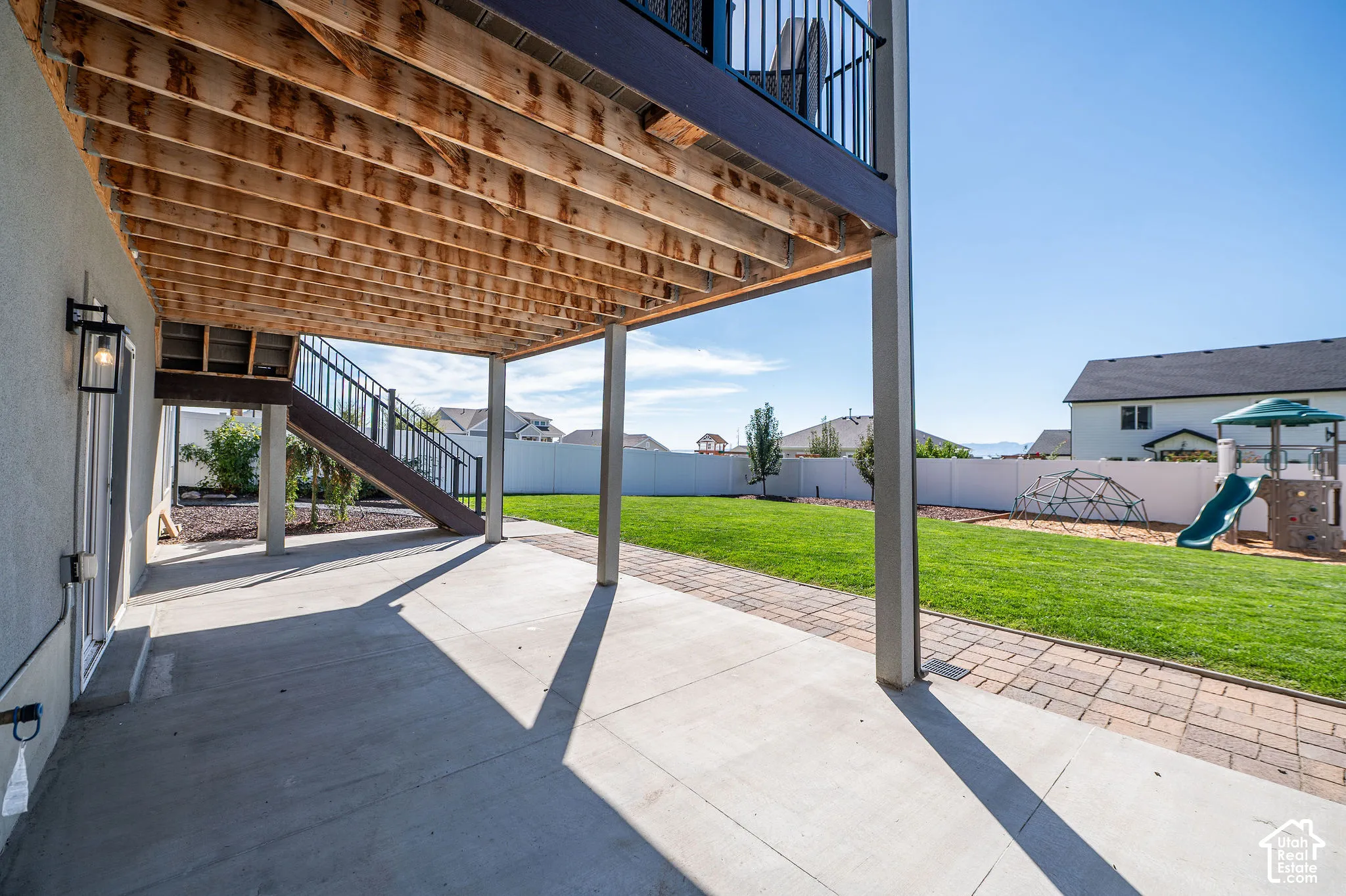 Expansive concrete patio with overhead deck structure, leading to a large grass lawn