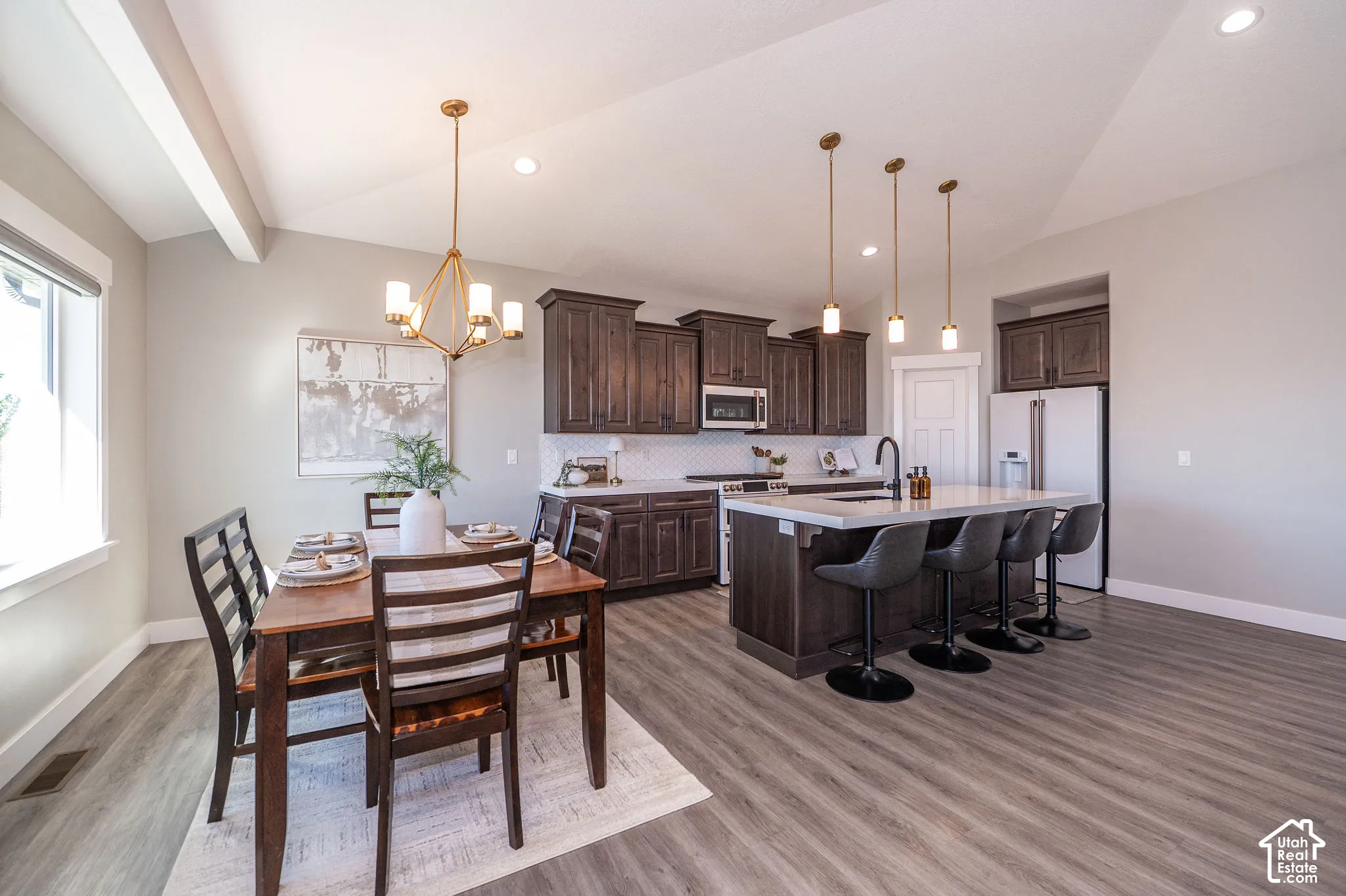 Open-concept living space featuring wood-finish flooring, dark wood cabinetry, a central kitchen island with seating, a tile backsplash, and recessed lighting