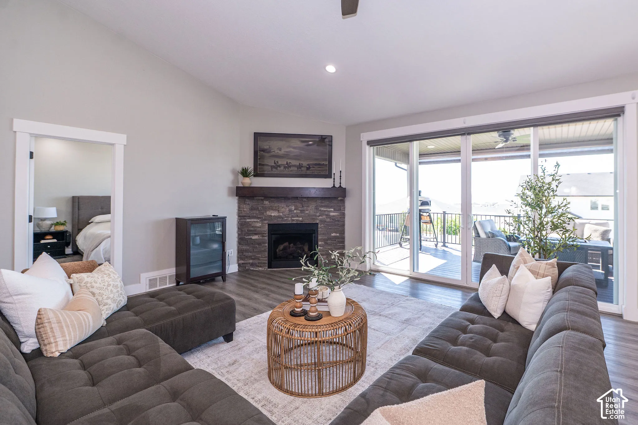 Vaulted ceiling with recessed lighting, stone-clad fireplace with wood mantel, sliding glass doors to outdoor deck, wood-finish flooring