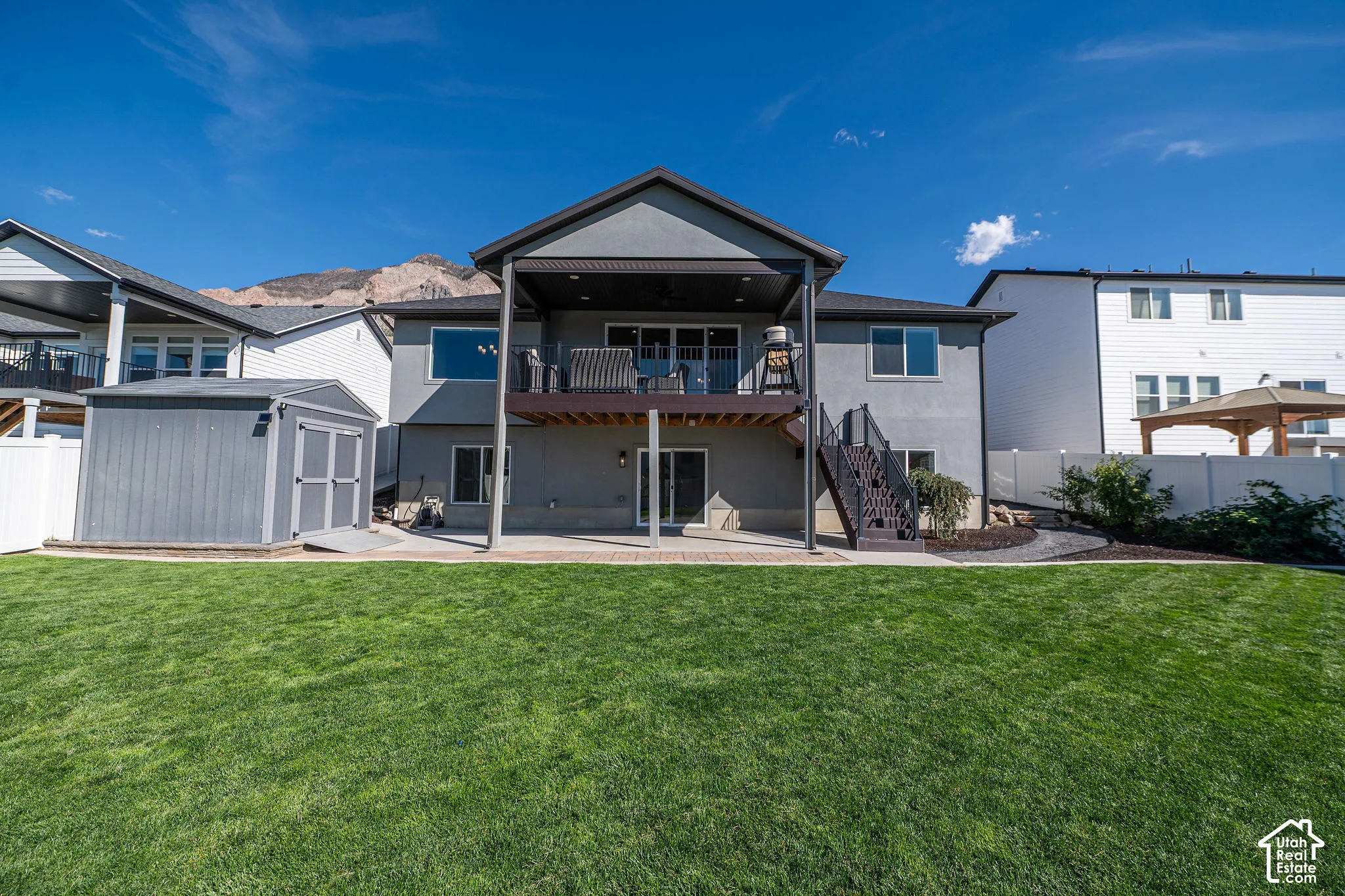 Expansive green lawn with a two-story residence featuring a covered upper-level deck and a lower-level patio