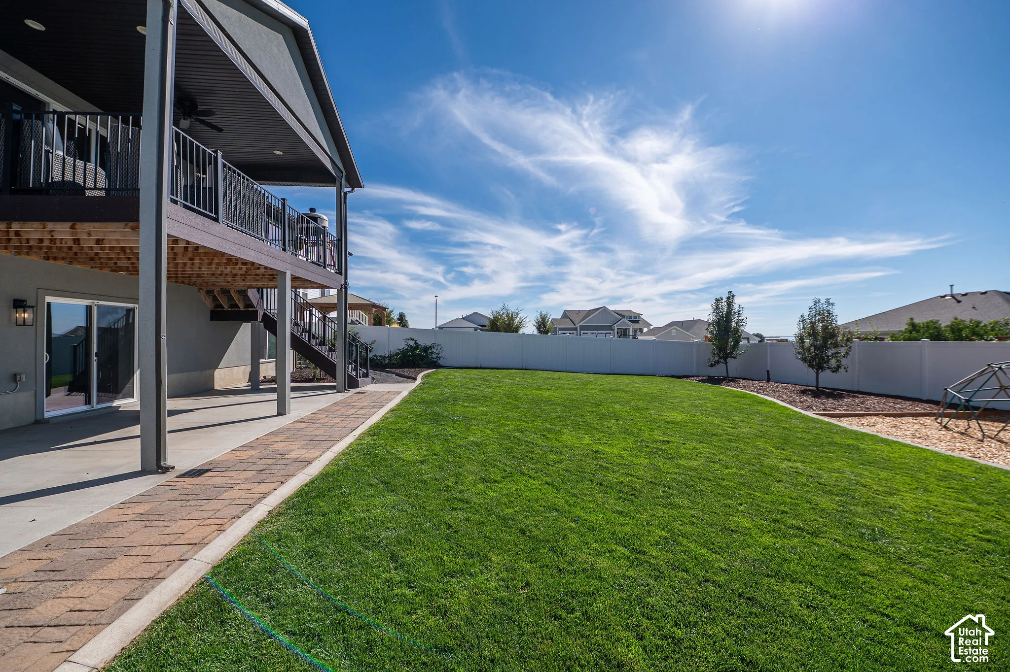 Expansive backyard featuring a green lawn, a multi-level deck with metal railings, a ground-level patio, and a privacy fence