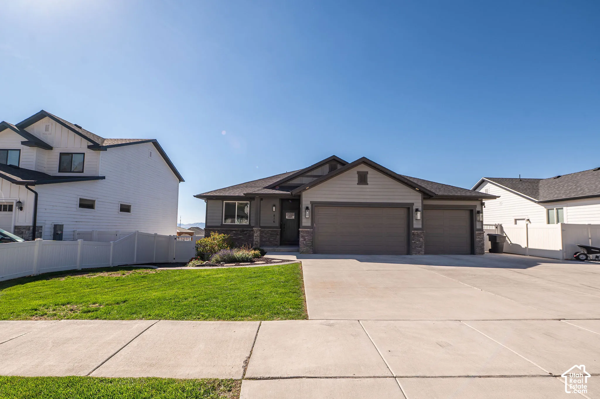 Contemporary ranch-style residence featuring a stone and siding exterior, an attached two-car garage, a concrete driveway, and a manicured lawn with mature landscaping