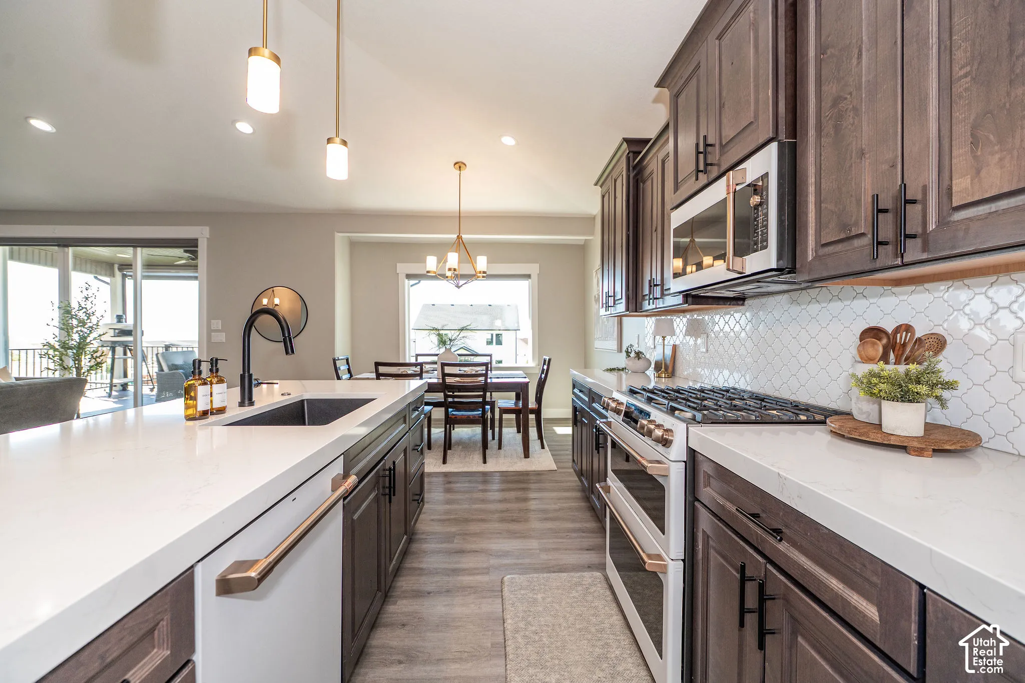 Kitchen featuring dark wood-finish cabinetry, white quartz countertops, a gas range with a double oven, a patterned tile backsplash, and a large central island with an undermount sink