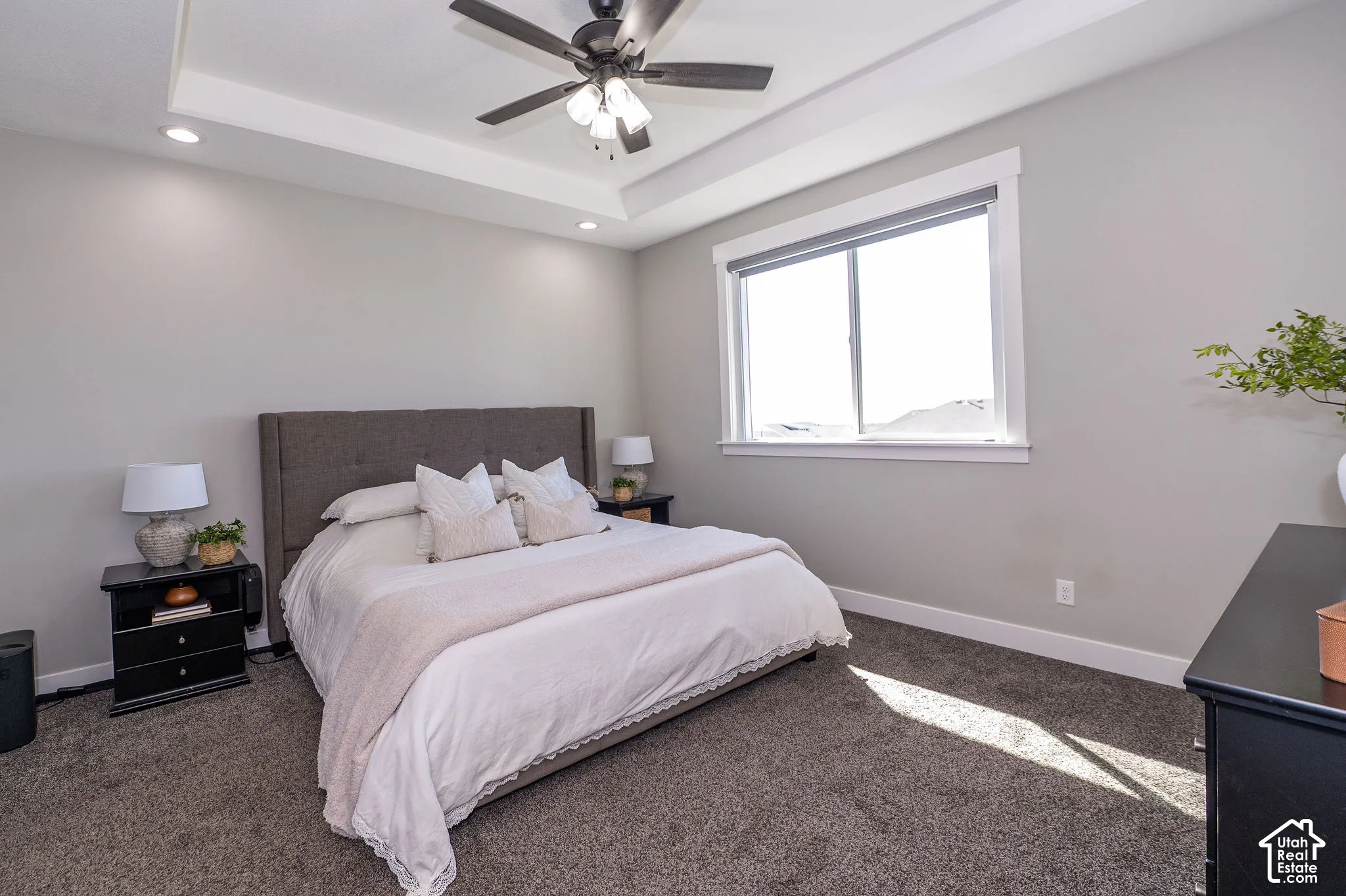 Tray ceiling with recessed lighting, ceiling fan, large window, and gray carpeting