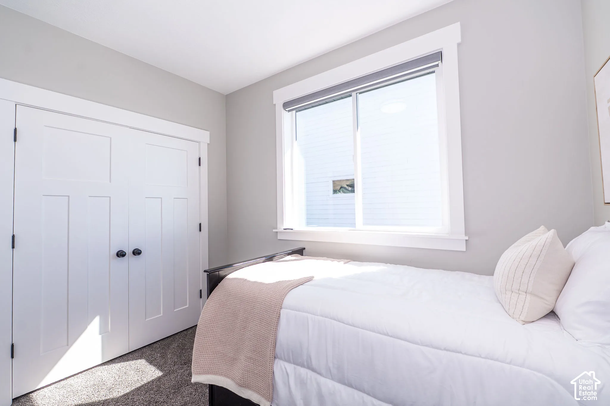 White trim window with roller shade, light gray wall, and white bi-fold closet doors with black hardware