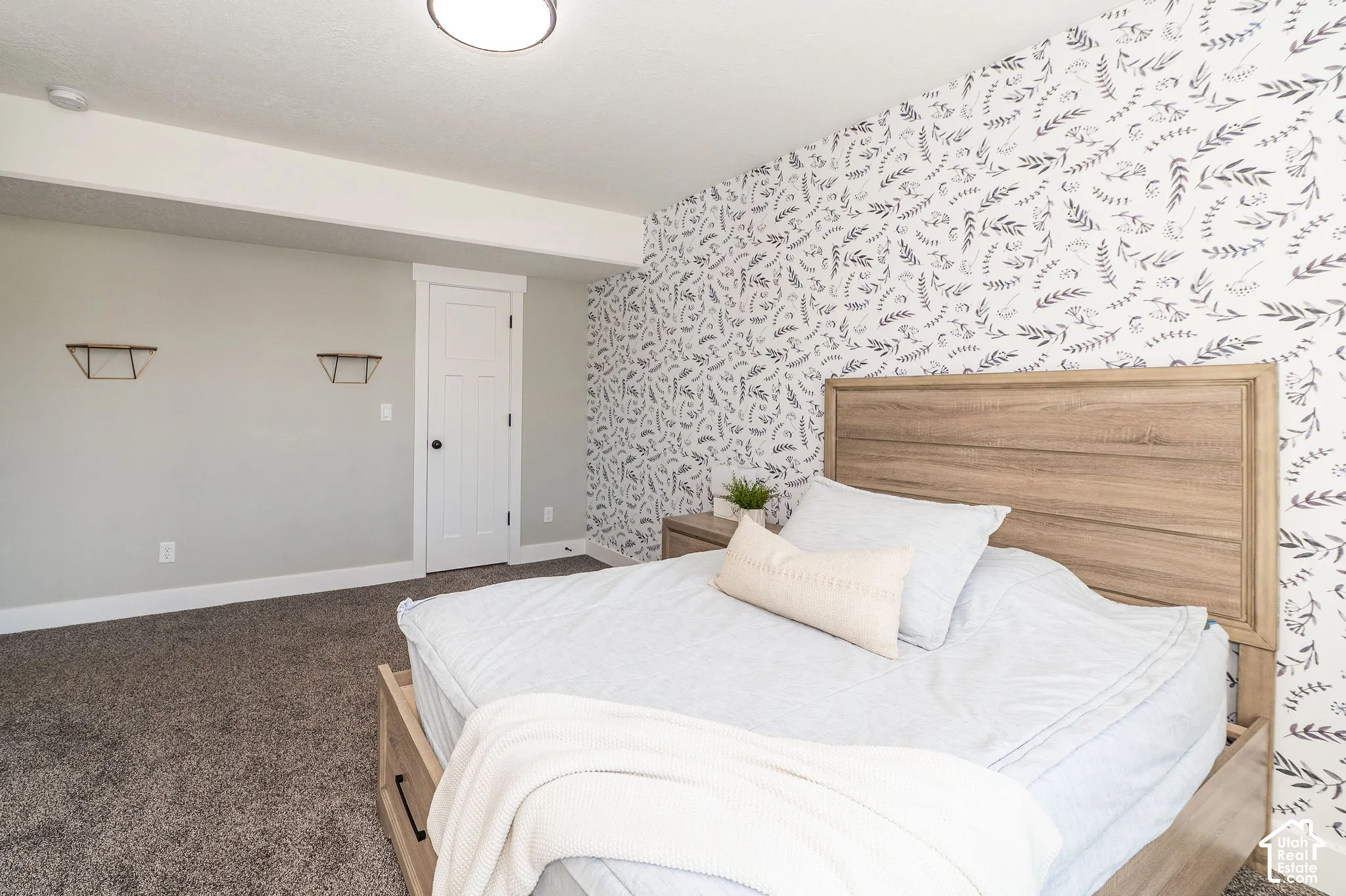 Wall-mounted shelving, wood-finish headboard, patterned accent wall, light gray wall paint, and recessed lighting