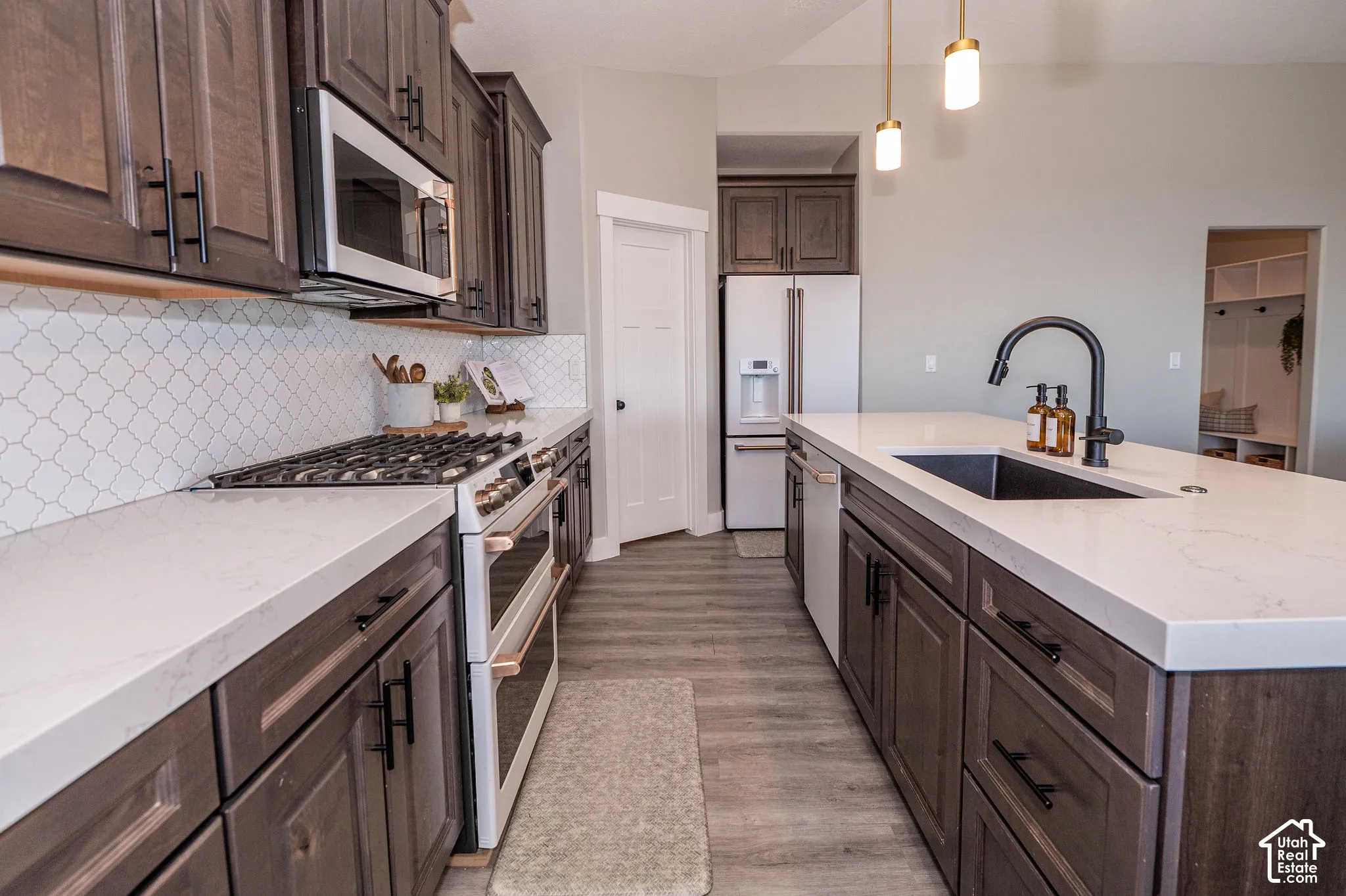 Kitchen featuring dark wood-finish cabinetry, light countertops, white arabesque tile backsplash, and stainless steel appliances