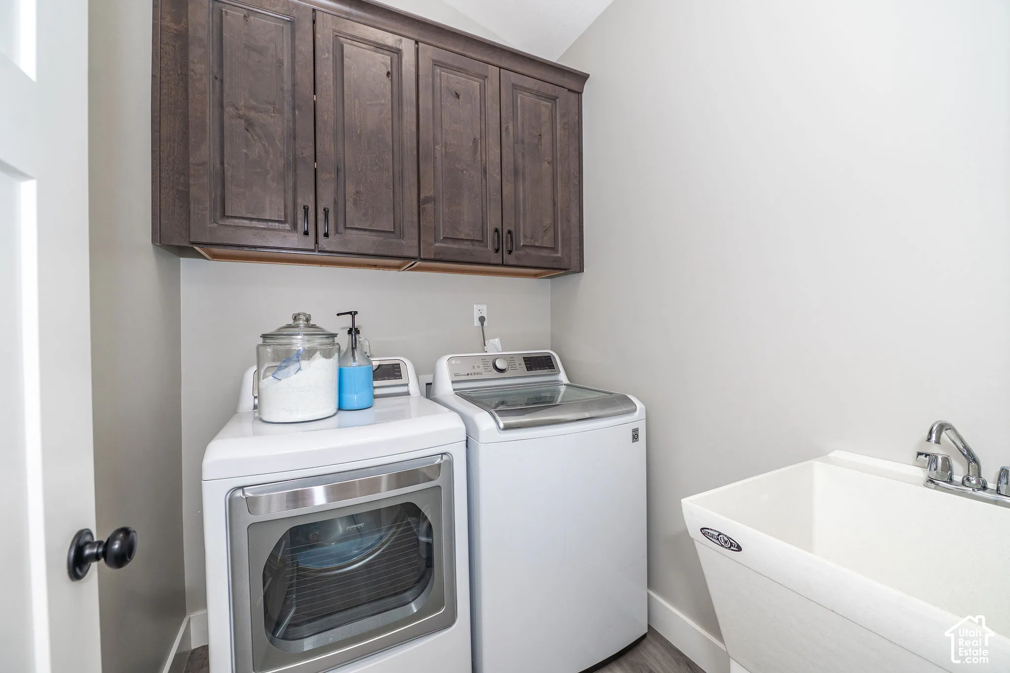 Upper dark wood-finish cabinetry, neutral wall paint, and a utility sink with a chrome faucet