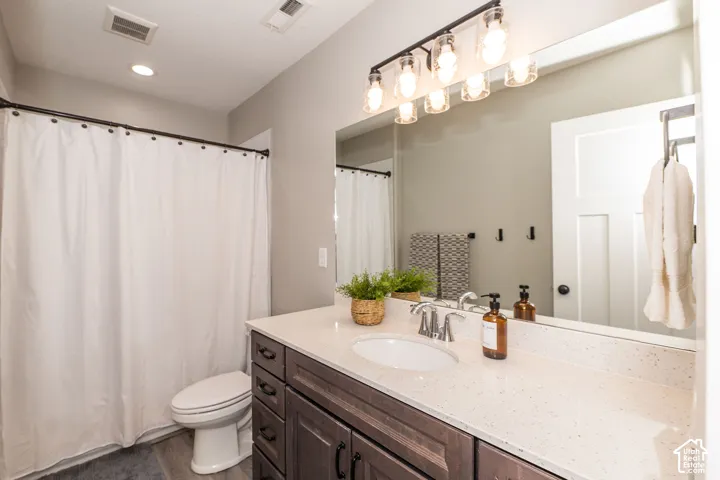 Wood-finish flooring, single vanity with a light-colored countertop, built-in cabinetry, and a toilet