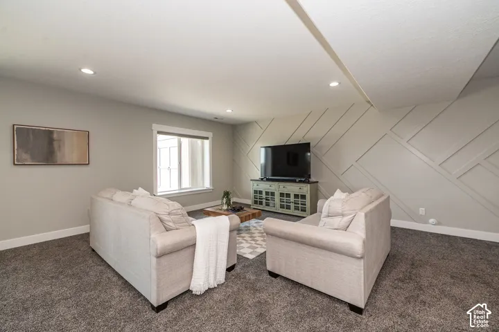Recessed lighting, wall-mounted television, built-in media console, accent wall with geometric paneling, and a large window