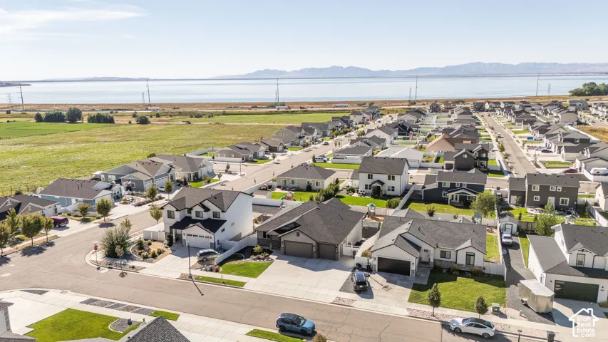 Expansive suburban development with manicured lawns and paved streets, featuring a prominent body of water and distant mountains