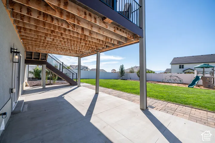 Expansive concrete patio with overhead deck structure, leading to a large grass lawn