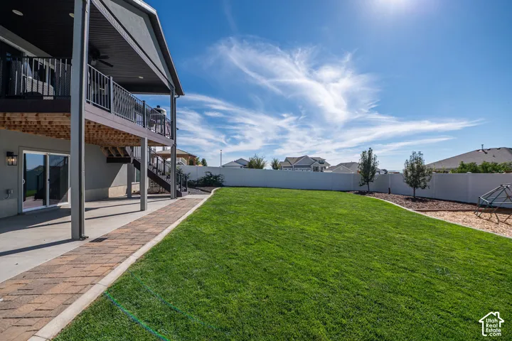 Expansive backyard featuring a green lawn, a multi-level deck with metal railings, a ground-level patio, and a privacy fence
