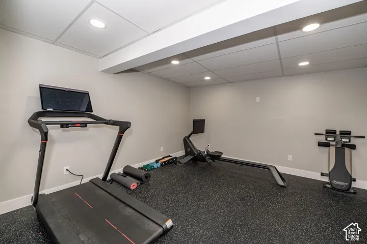 Recessed lighting illuminating a spacious room with a drop ceiling, featuring light-toned walls and durable rubber flooring