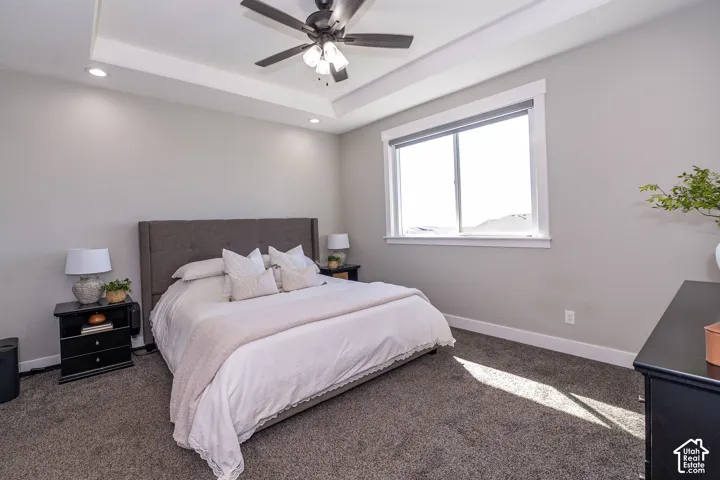 Tray ceiling with recessed lighting, ceiling fan, large window, and gray carpeting