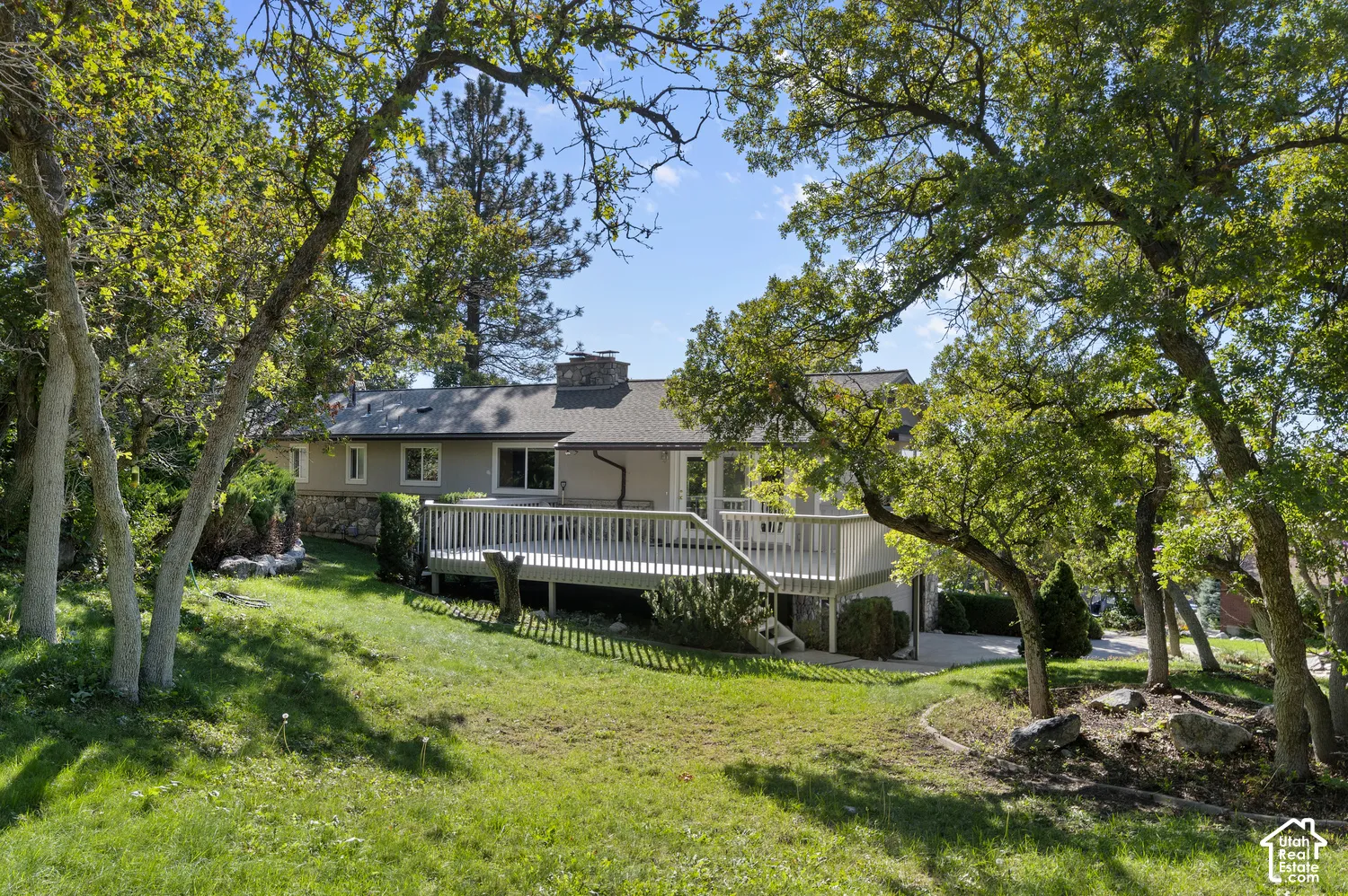 Expansive backyard featuring a manicured lawn, mature trees, a multi-level wood deck, and a stone facade