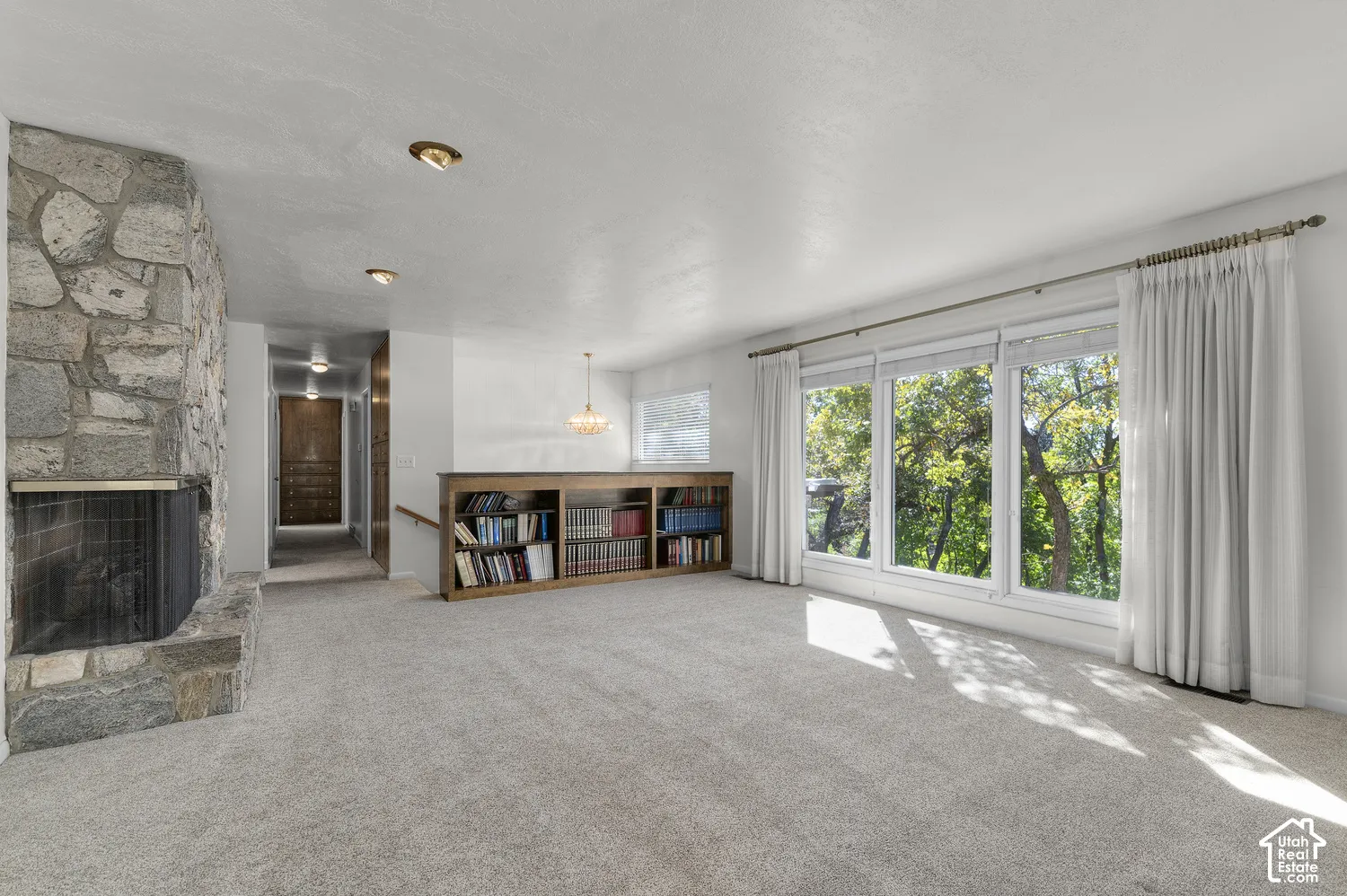 Stone-clad fireplace feature, large picture windows, built-in wooden shelving, recessed lighting, and a chandelier fixture
