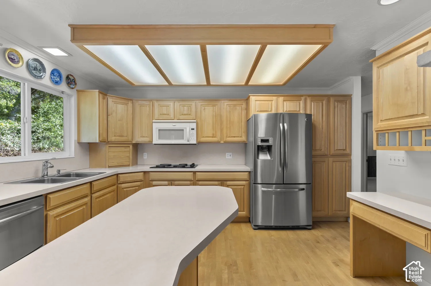 Light wood-finish cabinetry with white countertops, stainless steel appliances, and wood-finish flooring