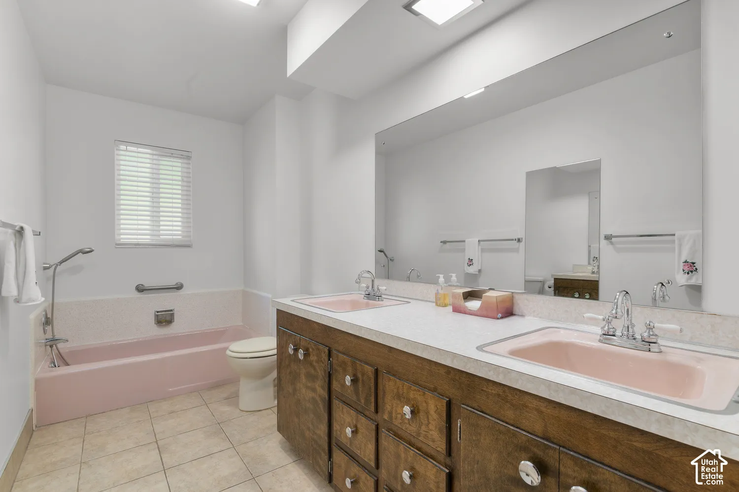 Dual vanity with wood-finish cabinetry, tile flooring, built-in bathtub, and an expansive wall mirror