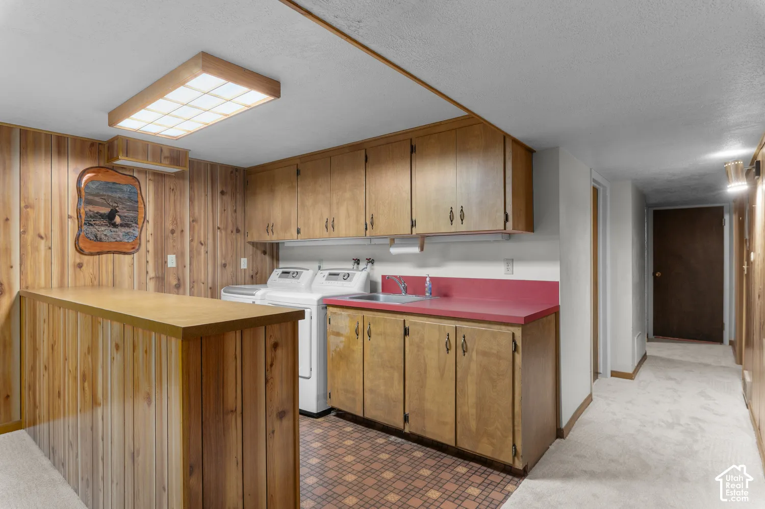 Laundry area with wood-paneled walls, built-in wooden cabinetry, a utility sink, and patterned floor tiling