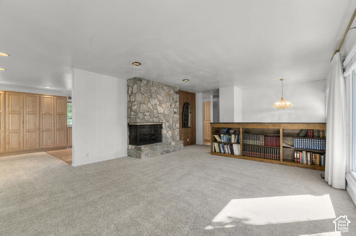 Stone fireplace with hearth, built-in shelving, recessed lighting, and wood-finish cabinetry