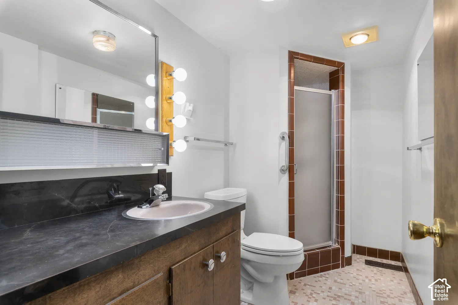 Vanity with a built-in sink, wall-mounted mirror with integrated lighting, and a walk-in shower with a glass enclosure