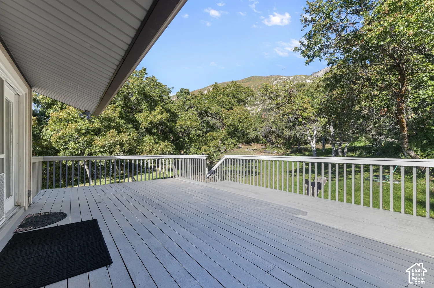 Expansive outdoor deck with railing, offering a natural treed backdrop and mountain scenery