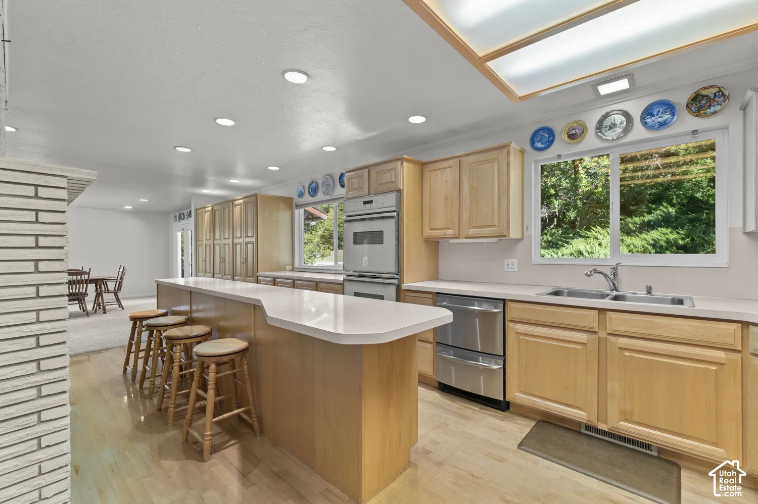 Expansive kitchen island with seating, stainless steel appliances, wood-finish flooring, recessed lighting, and a large window