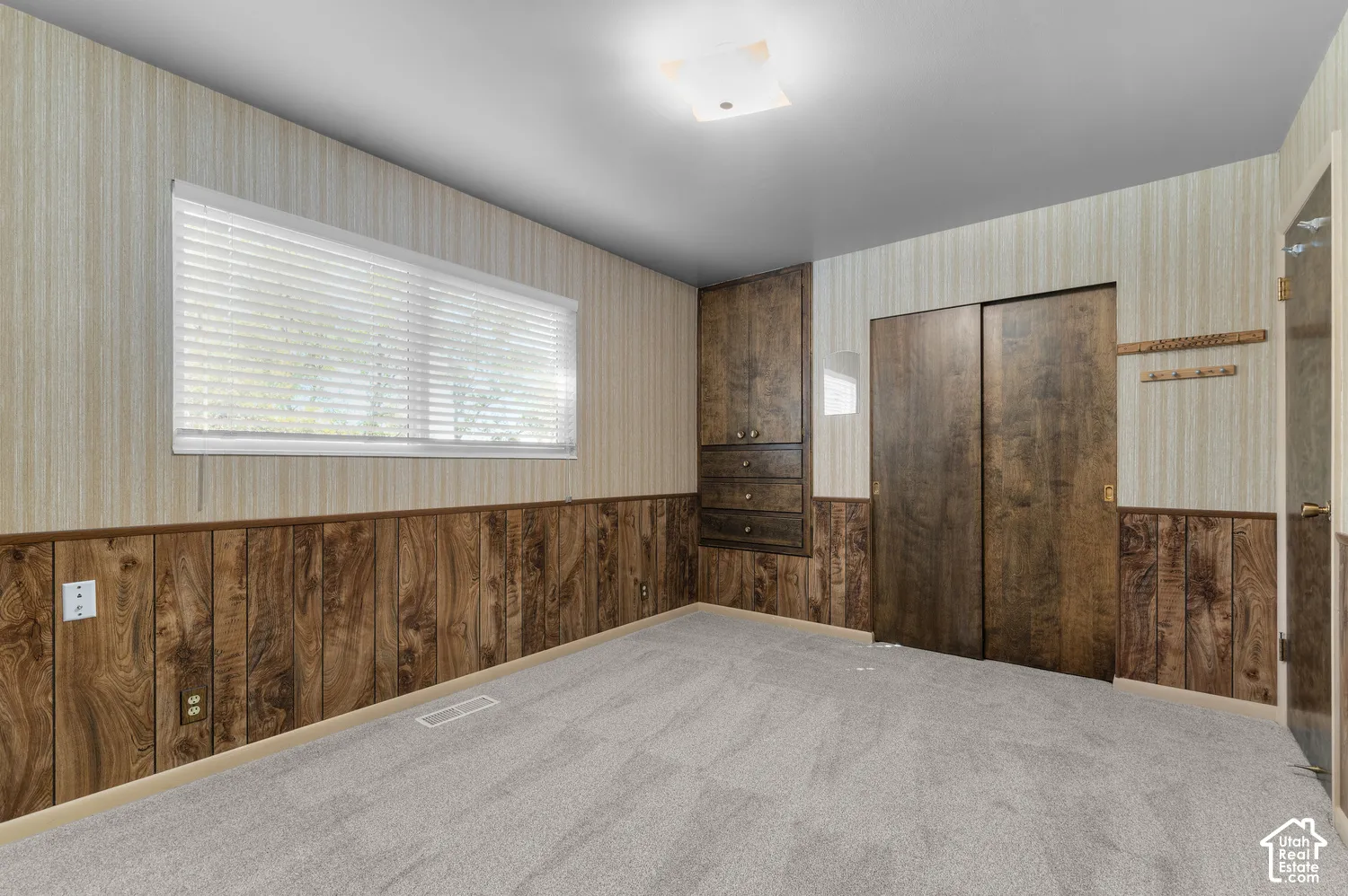 Plank wood-finish wainscoting, built-in cabinetry with drawers, wood-finish sliding doors, and light gray carpeting