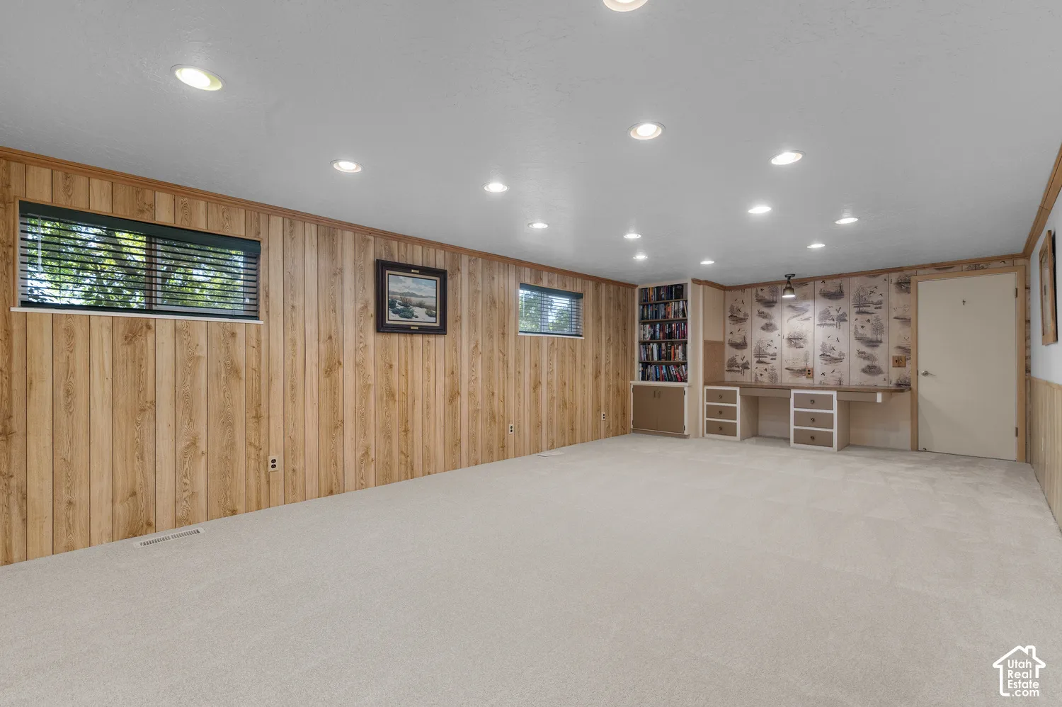 Recessed lighting illuminates the carpeted flooring and wood paneling