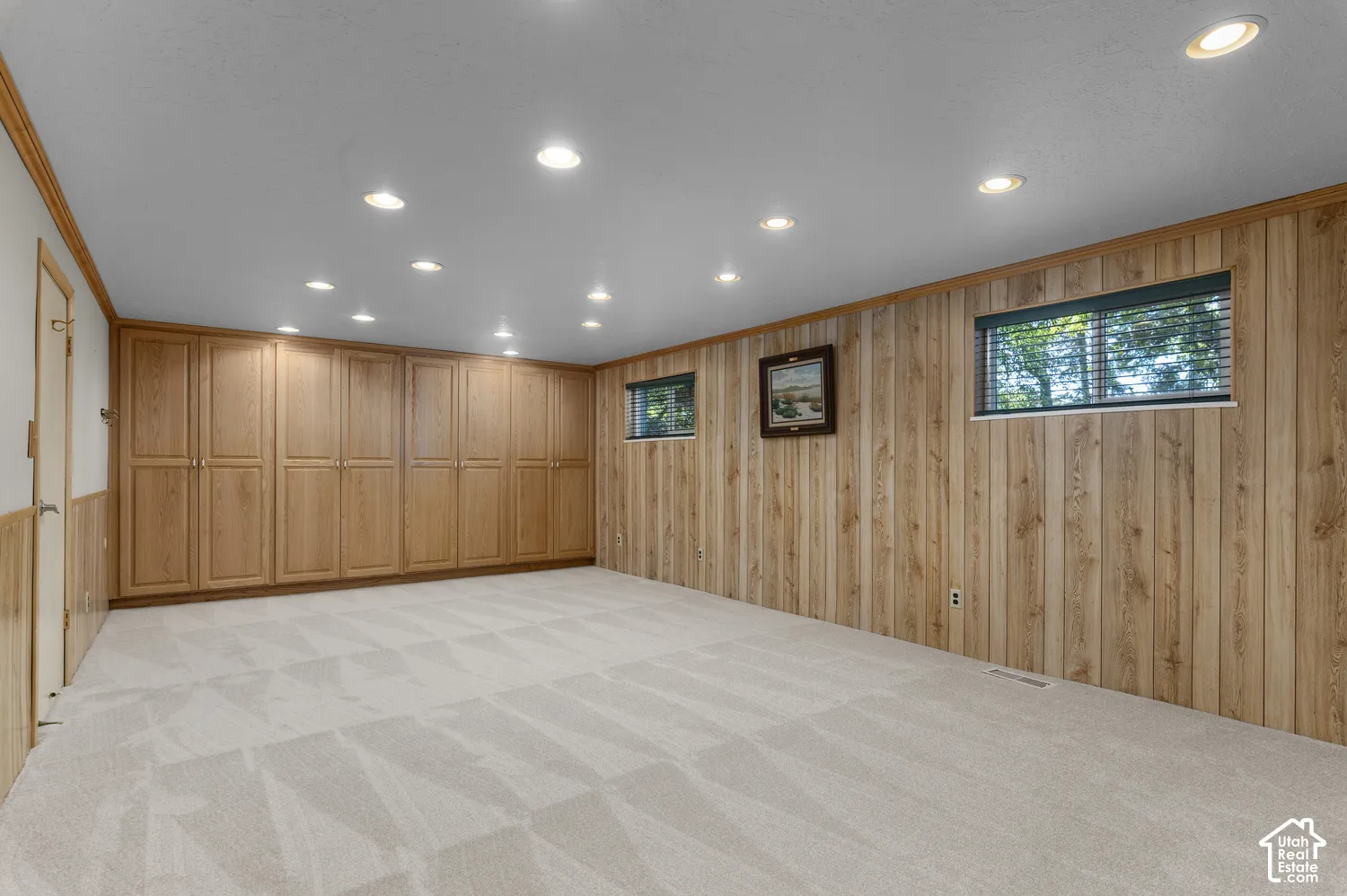 Recessed lighting, light wood-finish built-in cabinetry, wood-paneled walls, light-colored carpet, and transom windows